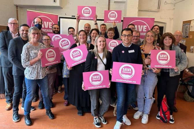 Save Birmingham campaign launch event. A number of people holding pink Save Birmingham signs and smiling are shown in the picture.